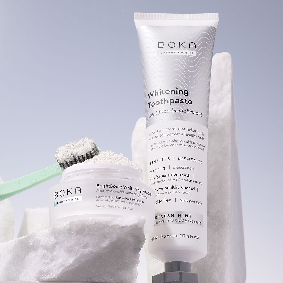 Boka whitening toothpaste and whitening powder with a green toothbrush on white marble blocks.