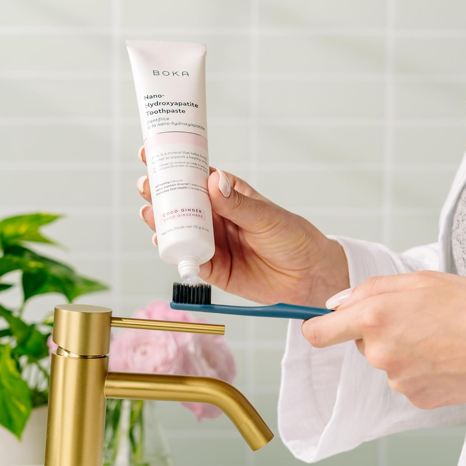 Person squeezing Boka toothpaste onto a Classic Toothbrush 4-Pack near a gold faucet.