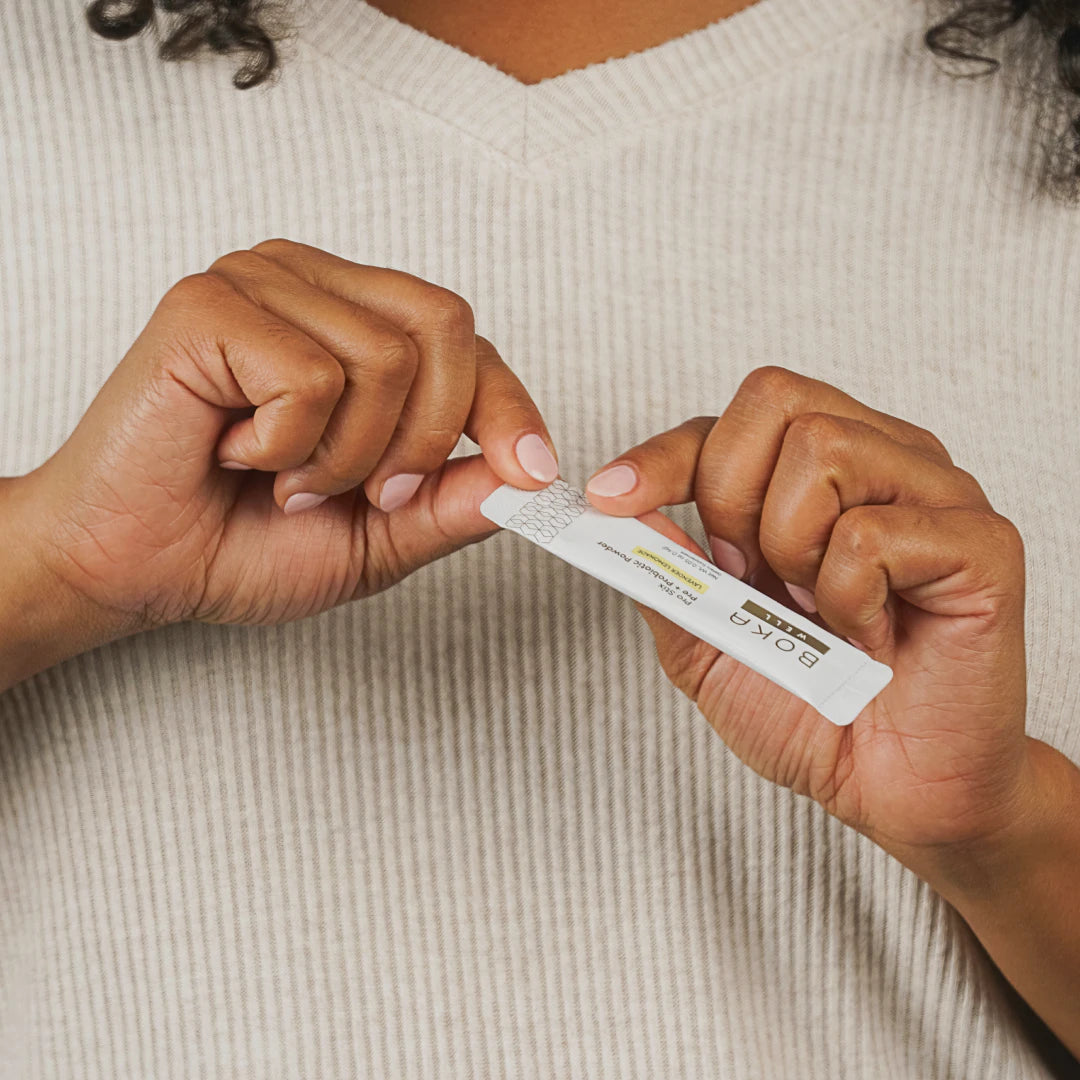 Hands tearing open a Boka toothpaste tablet packet, person wearing a beige ribbed shirt.