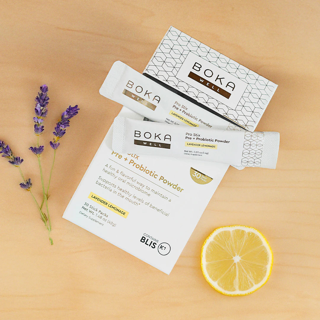 Boka probiotic powder packets with lavender sprigs and a lemon slice on a light wooden surface.