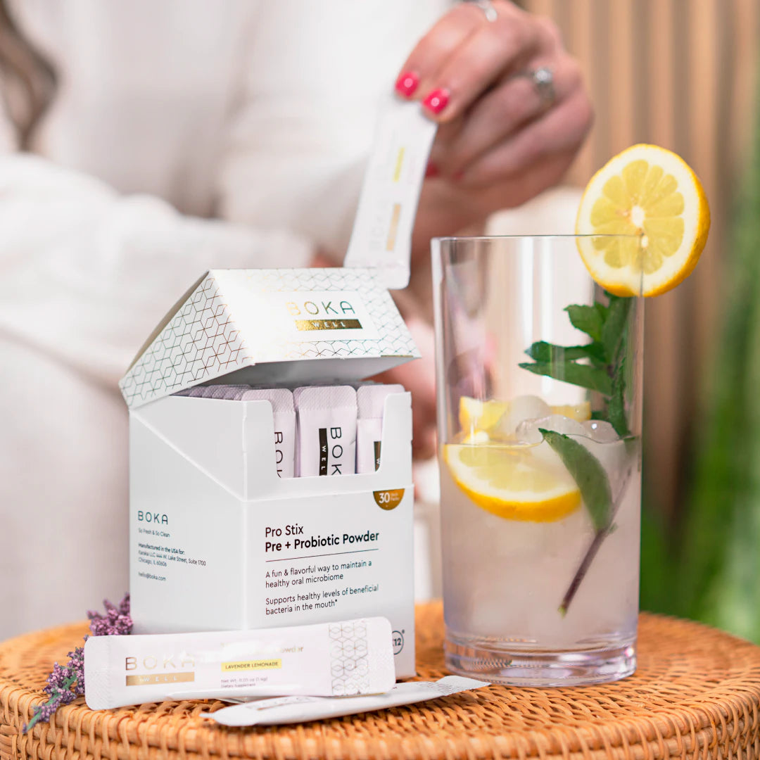 A hand pours powder from a Boka packet into a glass of lemon and mint-infused water.