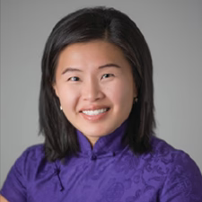 Woman with shoulder-length black hair smiles, wearing a purple patterned top against a gray background.