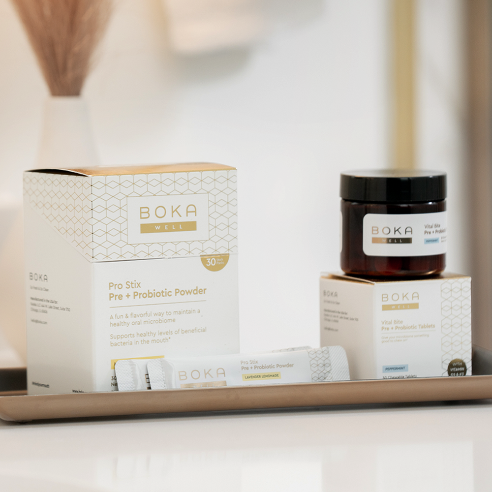 Boka Well probiotic products displayed on a tray, including powder sticks, a jar, and a box.