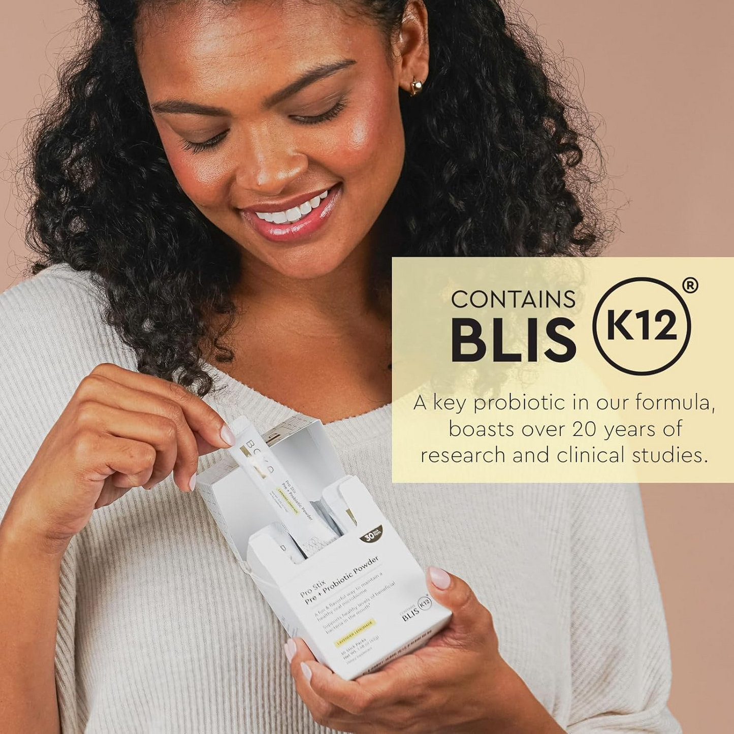 Smiling woman holds Pro Stix Pre + Probiotic Powder, highlighting oral probiotic benefits beside her.