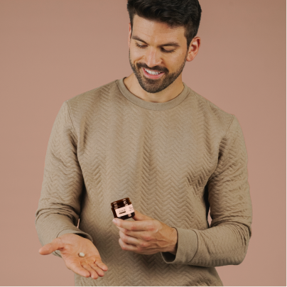 Man in beige sweater smiling while holding a pill bottle and pouring pills into his hand.